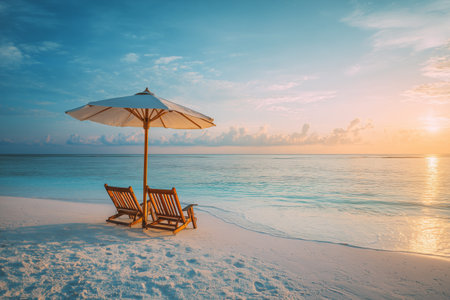 Two wooden loungers are placed under a white umbrella at the beach. The sunset casts a warm glow over the serene ocean, creating a peaceful atmosphere.の素材