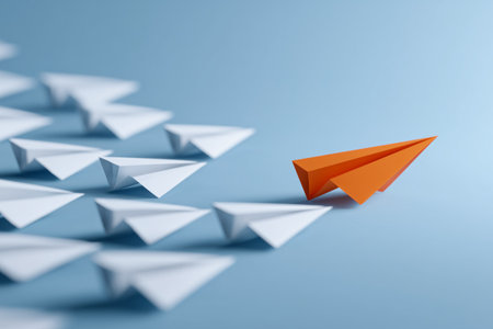 An orange paper airplane stands out among many white ones. The group is arranged artistically on a light blue background, creating a striking visual contrast.. Details matter.の素材