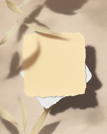 Textured paper in soft tones sits on a light-colored surface, surrounded by delicate dried leaves casting gentle shadows, creating an artistic composition.の素材