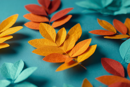 Bright orange and yellow leaves are artistically placed around a turquoise surface, creating a seasonal decoration. This display captures the essence of autumn.の素材
