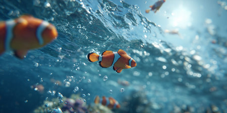 Schools of bright clownfish glide among sparkling waves and coral, showing their vivid patterns in a serene underwater environment during daylight.の素材