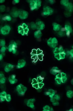 Small green clover shapes illuminated in a dark setting. These shapes are arranged randomly and create a vibrant display associated with a celebration in March.の素材