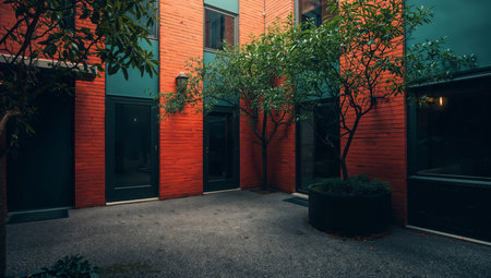 A courtyard with orange and gray walls features a round fountain in the center. Surrounding plants are placed in pots. A chair is nearby, and a building is visible in the background.の素材