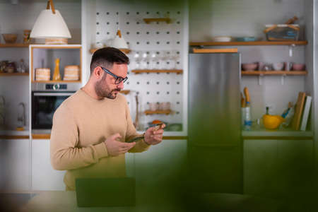 Confused and surprised attractive young caucasian man holding credit card calling bank. Failed...