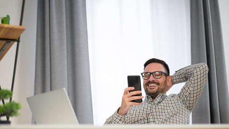 Handsome smiling young Caucasian man relaxing in office sending text message, checking social media,...
