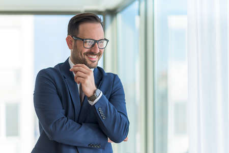 Smiling young manager standing in the office by the window talking on the phone. Portrait of...