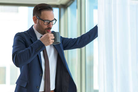 Smiling young manager standing in the office by the window talking on the phone. Portrait of businessman typing on the phoneの写真素材