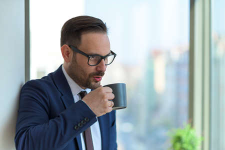 Portrait of the young caucasian manager enjoying moment of silent and drinking his coffee. break after a hard working dayの写真素材