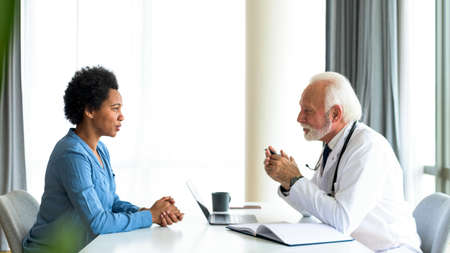Young african woman explaining medical symptoms to elderly experienced doctor. Concept of patient consultation with a doctor, looking for treatment advice.の写真素材