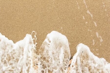 on a sunny day sea wave washes sand and legsの写真素材