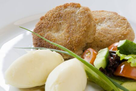 Fried cutlet with boiled potatoes and raw vegetables on a white plate