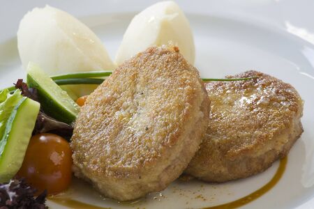 Fried cutlet with boiled potatoes and raw vegetables on a white plate