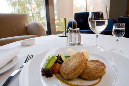 Fried cutlet with boiled potatoes and raw vegetables on a white plateの写真素材