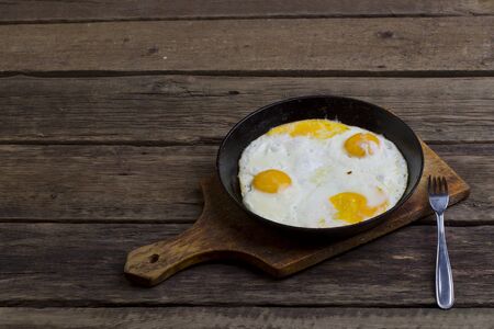 Fried eggs four eggs in a pan and fork on a cutting board on the boardsの写真素材