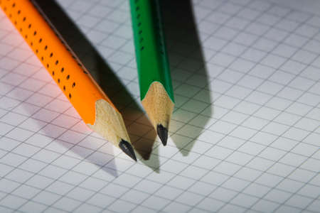 Two pencil, orange and green on a background of notebook sheet in the box, studio light illumination pointの写真素材