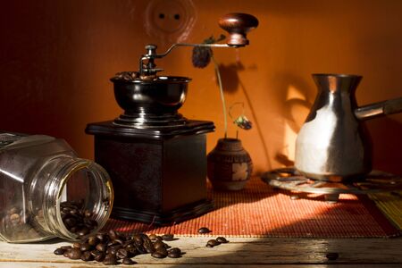 Grains of roasted Arabica coffee with coffee grinder, Turks, a glass jar on a bamboo mat and wooden table in natural light, the sun.の写真素材