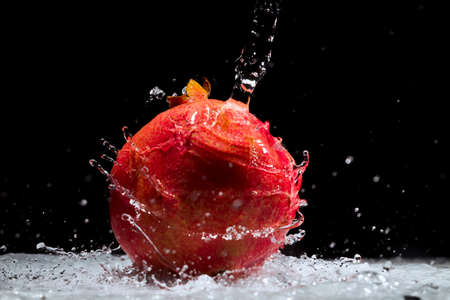 Pomegranate with drops and splashes water on black and white background, studio lightingの写真素材