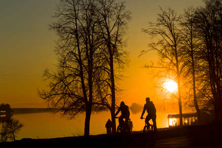 Spring sunset on the background of the river, trees, silhouettes, people, city, sunlightの写真素材