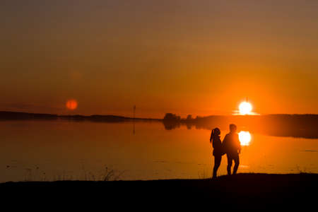 Spring sunset on the background of the river, trees, silhouettes, people, city, sunlightの写真素材