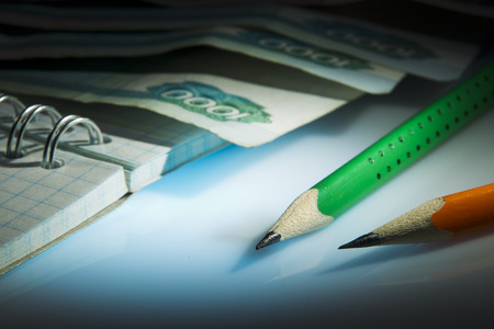 Two pencil, notebook, money lying on white acrylic, spot light studioの写真素材