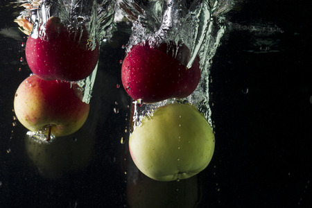 Apples falling into water on black background, studio lightingの写真素材
