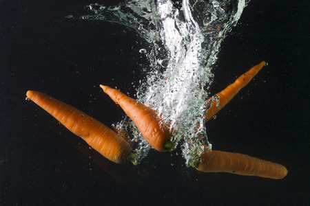 Carrot falling in water on a black background, studio lightingの写真素材