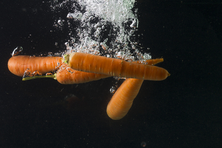 Carrot falling in water on a black background, studio lightingの写真素材