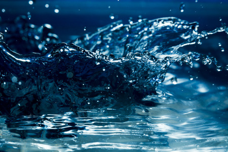 Flying, falling drops, sprays, splashes against the background of water in a cool blue tone, filmed...
