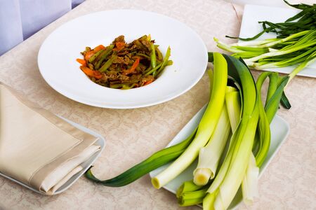 Meat fried with vegetables on the plate standing on the table, top view, studio lighting