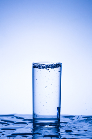 Drops, splashes, sprays, jets of water, a glass of water on a plastic background, studio lightingの写真素材