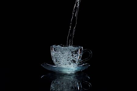 Water pours into a clear glass cup, black background, studio lightの写真素材