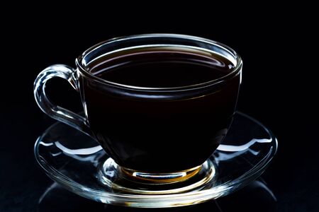 Hot black coffee smokes in a glass cup on a black background, studio lightの写真素材