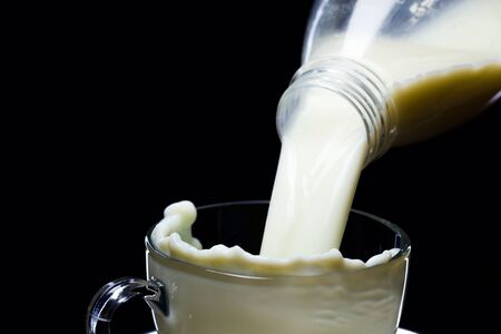 Natural milk is poured into clean glassware, black background, studio lightの写真素材