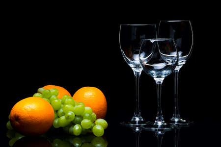 Three glasses for wine, a bunch of grapes and oranges on a black background, studio lightの写真素材