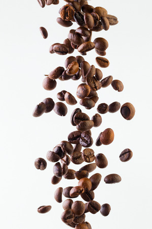 Grains of roasted coffee falling on white background, studio lightの写真素材