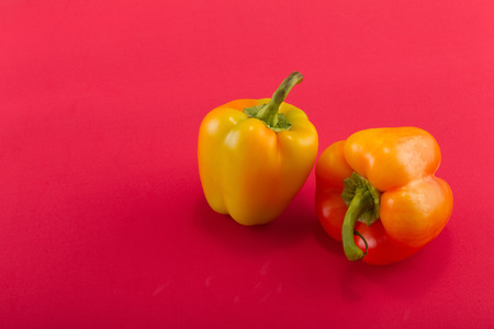 Sweet bellpepper. Two orange-yellow sweet bellpeppers on a red background. Two pieces. Studio light. Top viewの写真素材