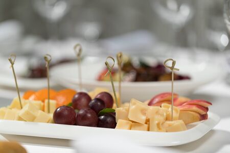 Banquet menu. Sliced â€‹â€‹fruit and cheese on a plate on a white tablecloth
