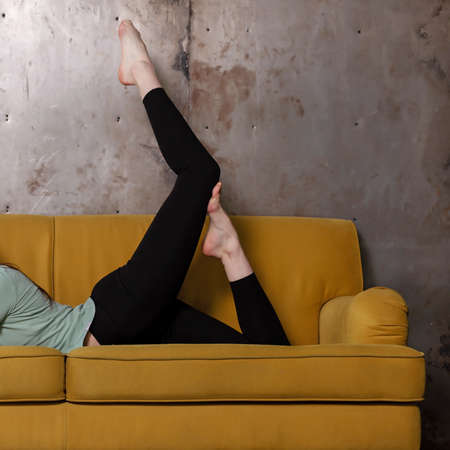 sporty young woman doing stretching exercise on the couch in living roomの写真素材