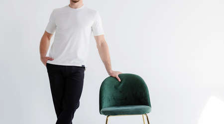 Man at home in blank t-shirt. Sitting in chair near the window at home thoughtful look. Mockup for printの写真素材