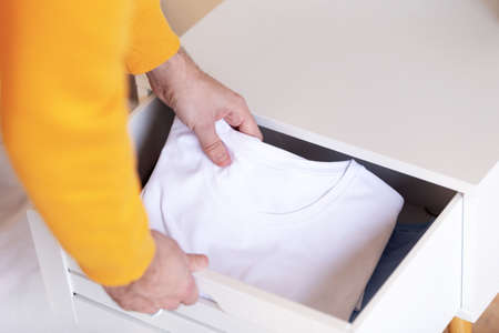 Hands take out a new t-shirt. Man picking shirt from clothes rack indoors. Fashionable wardrobeの写真素材