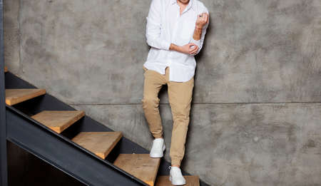 Man in white blank shirt. Standing on the stairs near the wall at home. Mockup for print