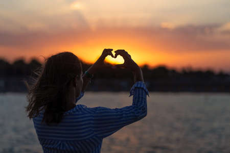 Woman making heart of hands at sea sunsetの写真素材