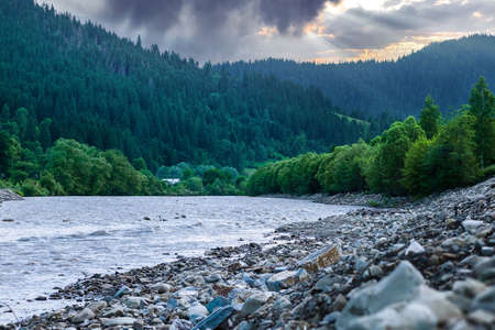 Clear river with rocks leads towards mountains lit by sunsetの写真素材
