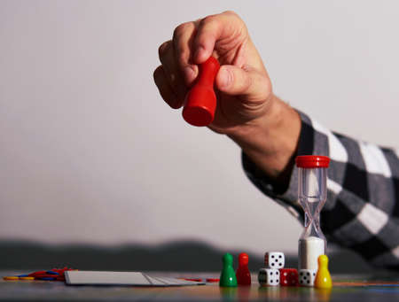 Your move - board game concept. Hand holding game figure in the air - making move. Board game field, many figures dark blurred backgroundの写真素材