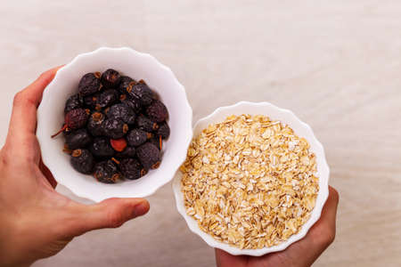 Man holding bowl of healthy oatmeal with dried fruits. Indoors, top view, sportswearの写真素材