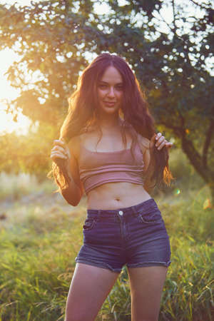 Beautiful woman enjoying the summer sun outdoors in the park. Dressed jeans shorts and beige top in golden hourの写真素材