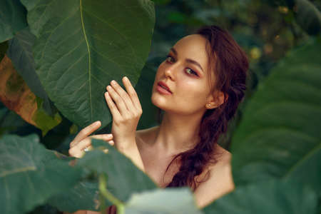 Woman face in green leaves enjoying nature. Portrait of beautiful woman with healthy glow smooth skin with natural green palm leaf. Cosmetology concept, free space for textの写真素材
