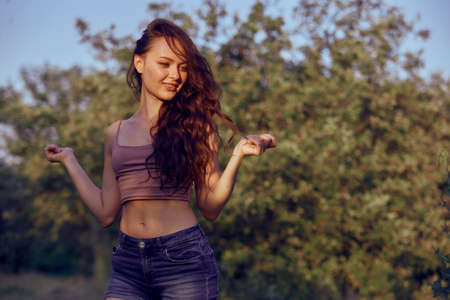 Beautiful woman enjoying the summer sun outdoors in the park. Dressed jeans shorts and beige top in golden hourの写真素材