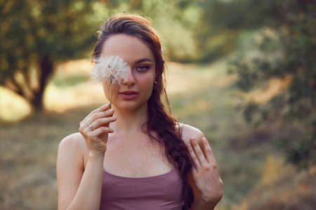Beautiful woman hold near face dandelion in the park. Free space for textの写真素材
