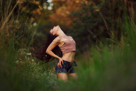 Sexy woman posing in a field in the grass rays of the sunset. Lifestyle on nature dressed in jeans shorts and beige top in golden hour. Romantic autumn mood, long tall grass in the meadowの写真素材